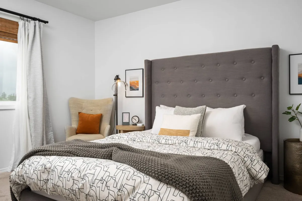 A calm, restful bedroom with a tufted headboard bed, an armchair tucked for reading, soft decorative pillows, a floor lamp, and soothing wall art. The ambiance is peaceful, evoking a sense of comfort and personal retreat.