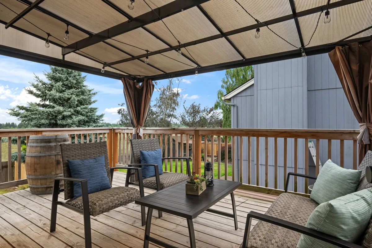 A covered outdoor seating area on a balcony or deck, complete with a wooden railing, a cozy table with a planter, and tranquil surroundings. The inviting setup suggests a perfect spot for morning coffee, reading, or intimate evening conversations.
