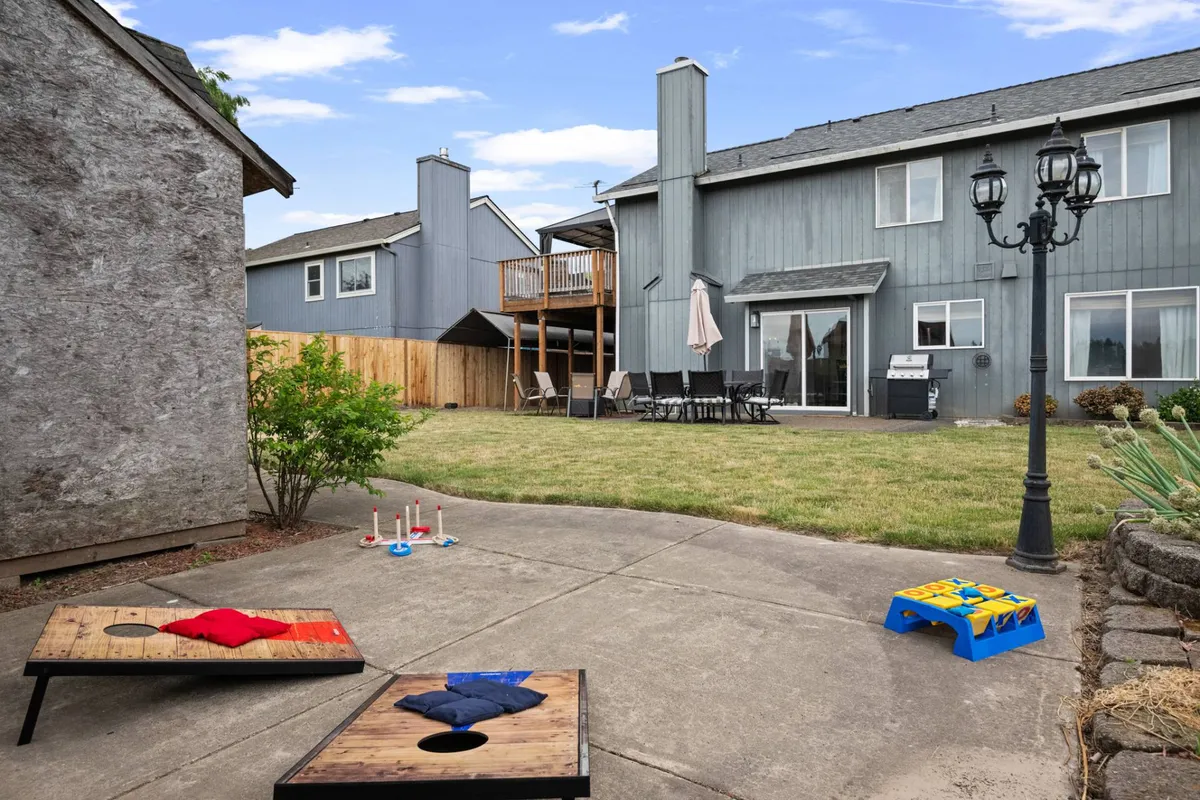 A vibrant backyard scene featuring a spacious seating area, a setup for cornhole game, and an outdoor grill. The area is enclosed by a fence and surrounded by greenery, creating a safe and playful environment for children and pets, as well as a comfortable spot for adults to gather.