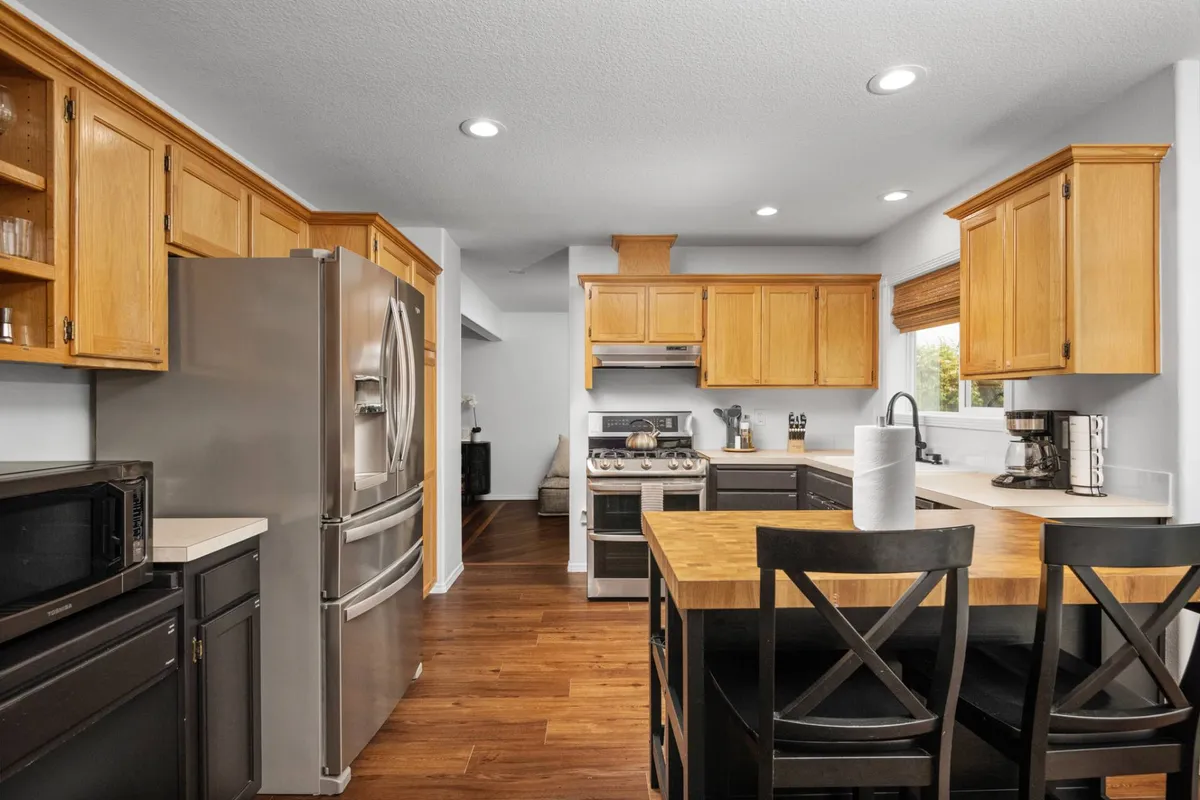 The kitchen features a central island, stainless steel appliances, and warm wooden cabinetry, all illuminated by natural light from a large window. The inviting atmosphere hints at both casual and festive family gatherings.