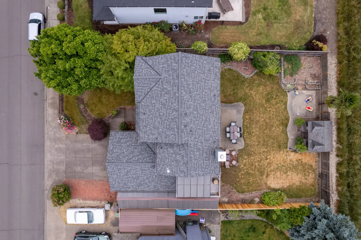 A spacious backyard featuring a well-maintained lawn, a variety of trees, an outdoor seating area, and a dedicated children's play area. The setting is relaxed and family-friendly, with the entire space visibly enclosed by fencing that ensures pet safety.