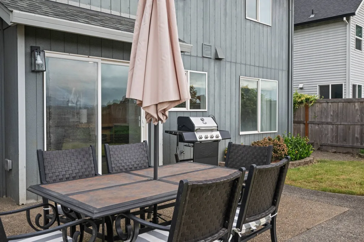 An outdoor dining table with a parasol sits on a patio next to a grill, set for a meal and surrounded by greenery. The area looks ready for an al fresco family dinner or a relaxed barbecue after a day of exploration.