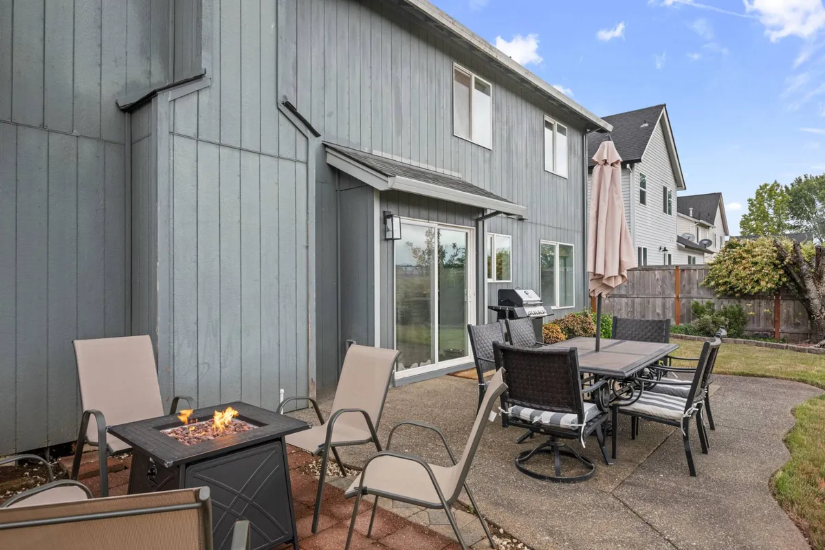 An inviting outdoor living space with a fire pit, a dining table set under an umbrella, and lounge chairs, all thoughtfully arranged for relaxation and socializing. The ambiance is comfortable, ideal for al fresco meals or unwinding by the fire as day turns to night.