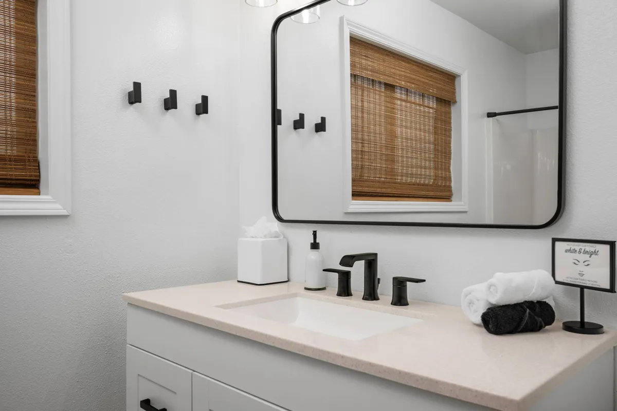 A bright, modern bathroom with a large mirror, sleek black fixtures, and abundant natural light streaming in from the window. The space exudes a spa-like tranquility, ideal for personal grooming and relaxation.