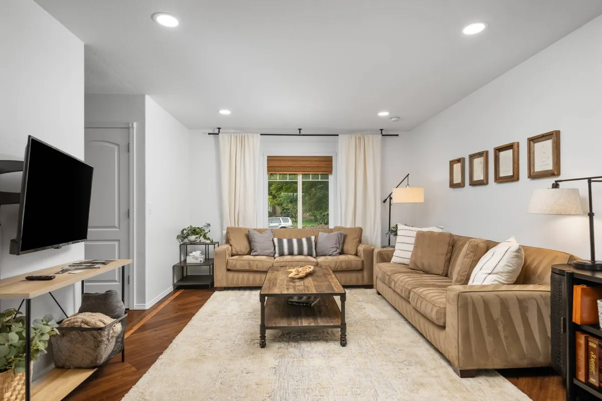 A warm, inviting living room featuring a plush sofa and tastefully decorated coffee table, with ample natural light streaming in through a large window. The space is arranged for relaxation and togetherness, perfect for watching TV, reading, or enjoying cozy conversations.